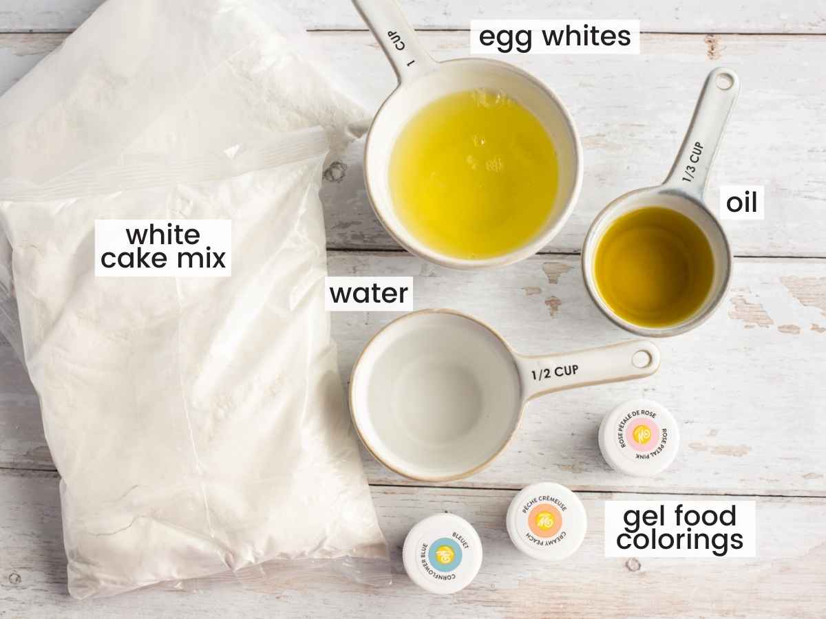 Ingredients needed to make unicorn cake including 2 packages of white cake mix, egg whites, oil, water, and gel food colorings.