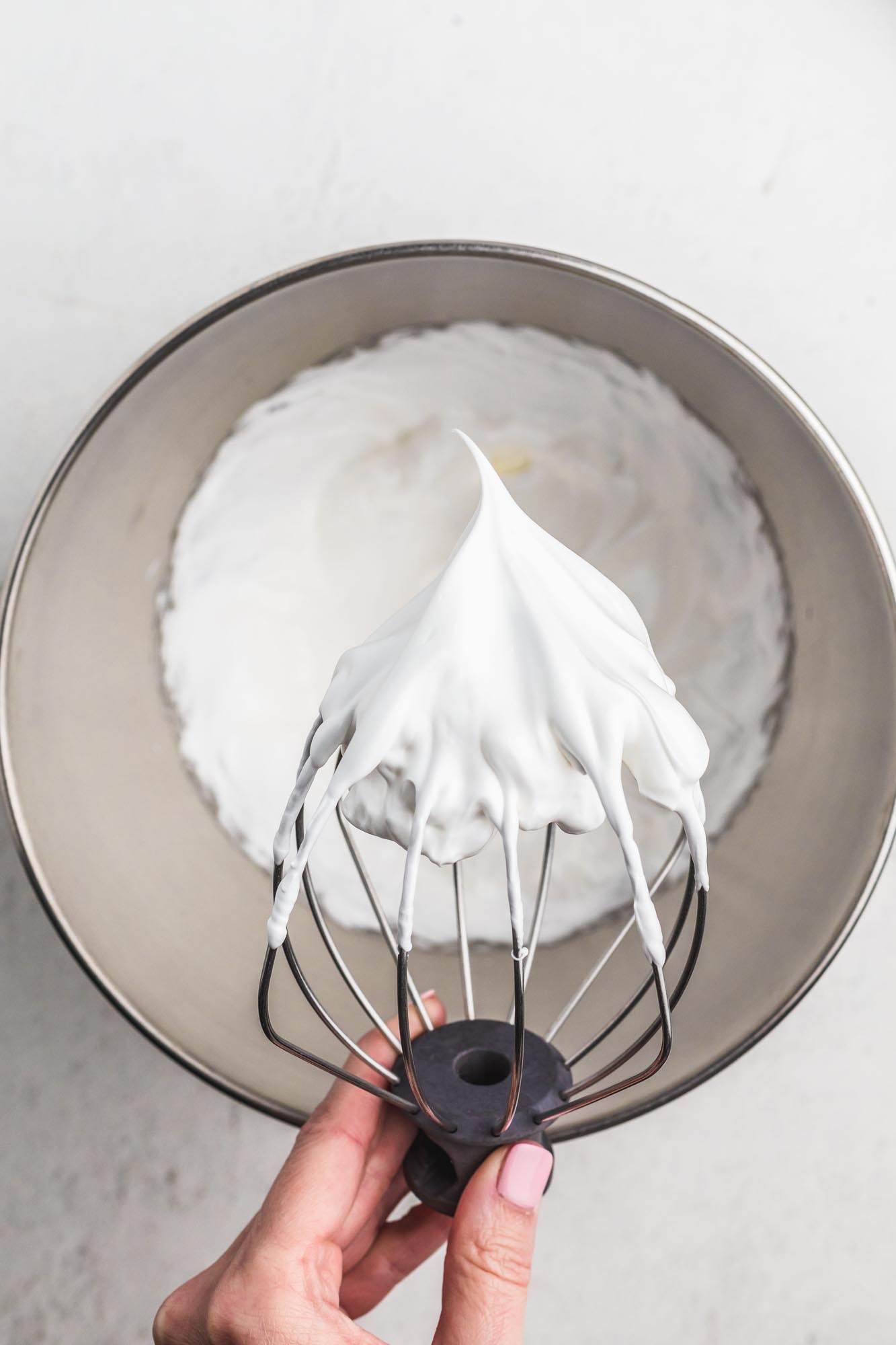 Holding a whisk beater with whipped white meringue over a metal bowl
