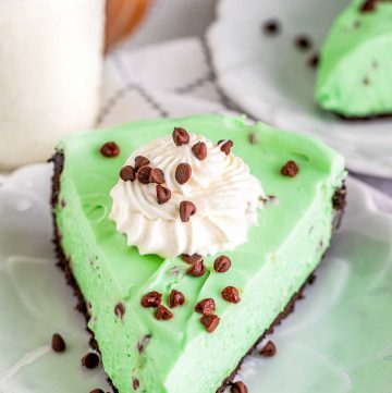 A slice of mint chocolate cheese cake plated, topped with whipped cream and chocolate chips