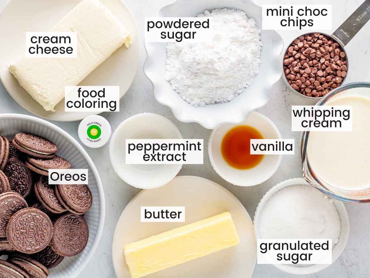 Ingredients needed to make mint chocolate cheesecake including Oreos, butter, cream cheese, powdered sugar, mini chocolate chips, heavy whipping cream, granulated sugar, vanilla extract, peppermint extract, and green food coloring.