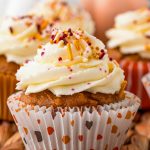 Close up shot of a pumpkin cupcake with vanilla frosting and sprinkles