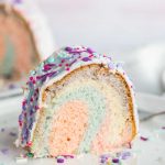 Slice of colorful unicorn cake with glaze and sprinkles on a small white plate
