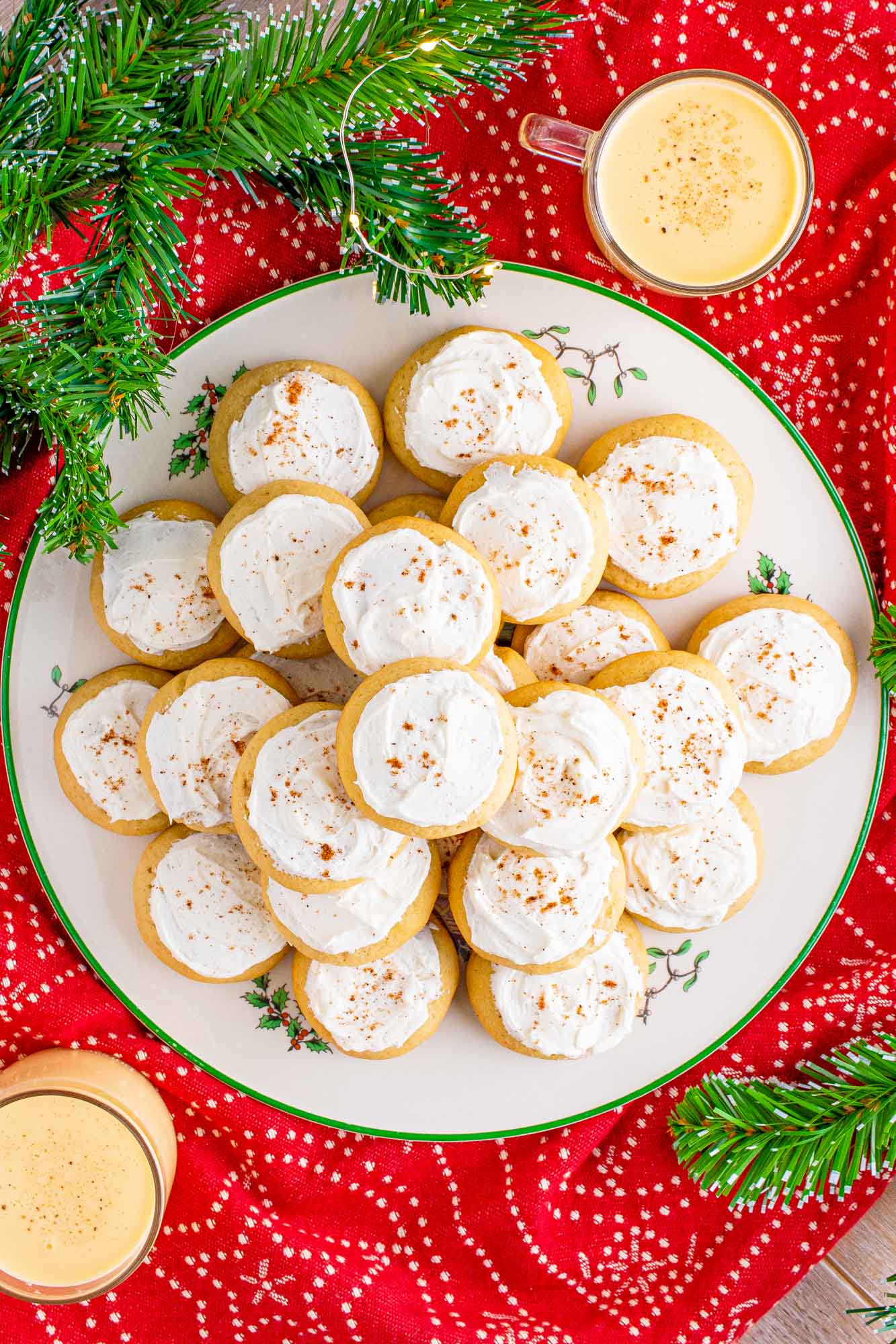 a round christmas plate filled with small eggnog cookies with white icing next to two mugs of eggnog