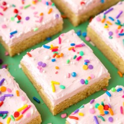 Sugar cookie bars with pink frosting and rainbow sprinkles on a green background