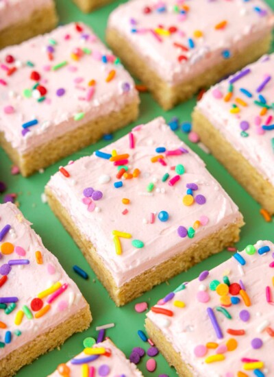 Sugar cookie bars with pink frosting and rainbow sprinkles on a green background