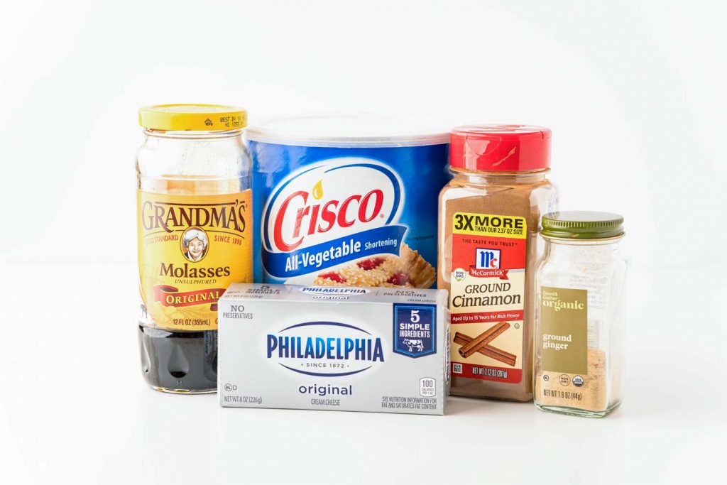 ingredients needed to make gingerbread cookie bars next to each other . Includes molasses, crisco, cream chease, and spices
