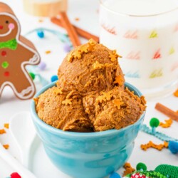 a blue bowl with three scoops of gingerbread cookie dough topped with gingerbread man sprinkles. The bowl is surrounded by christmas themed decorations.