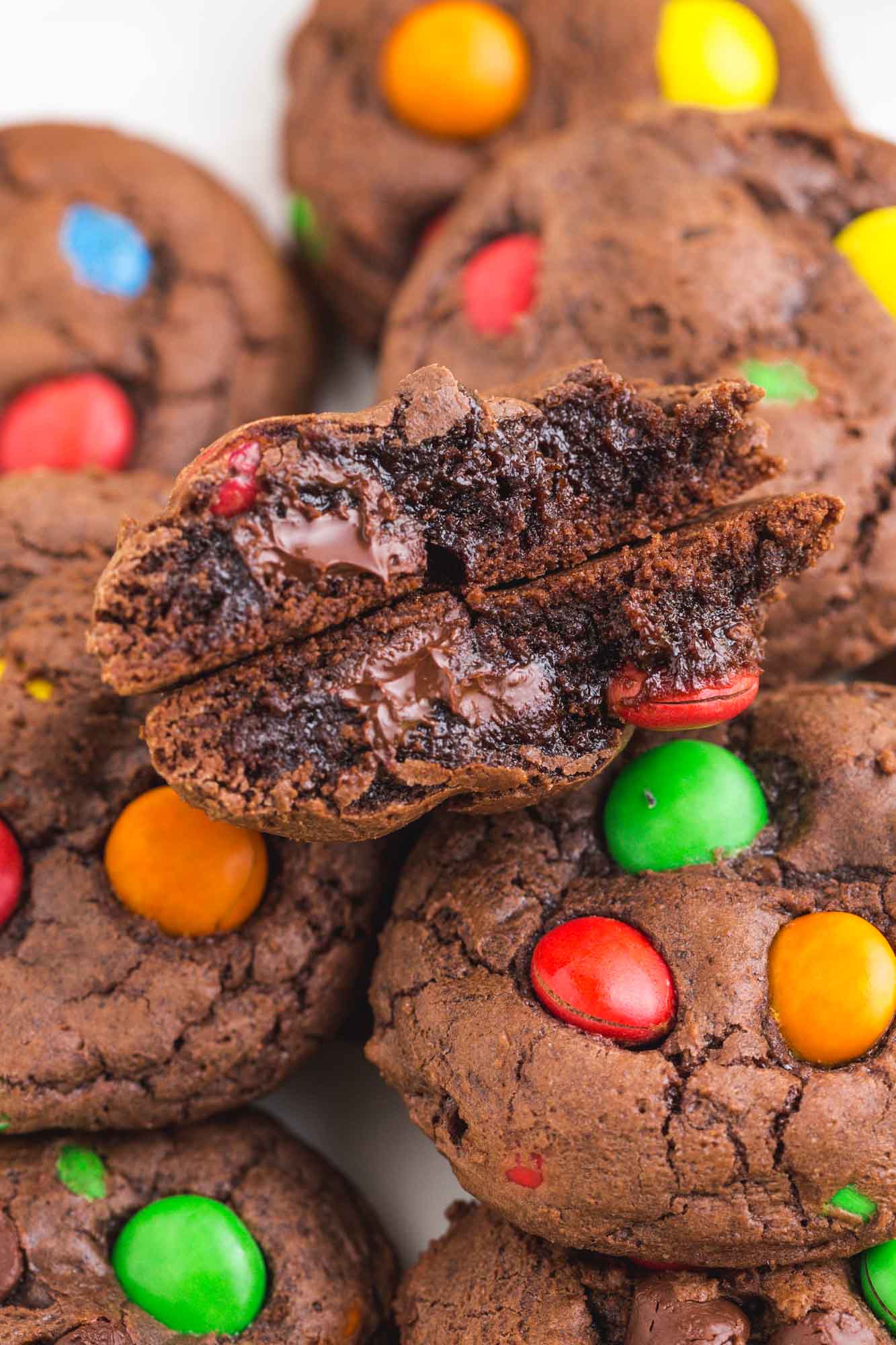 a closeup view of m&ms brownie cookies, one is broken in half to show the gooey, melty inside.