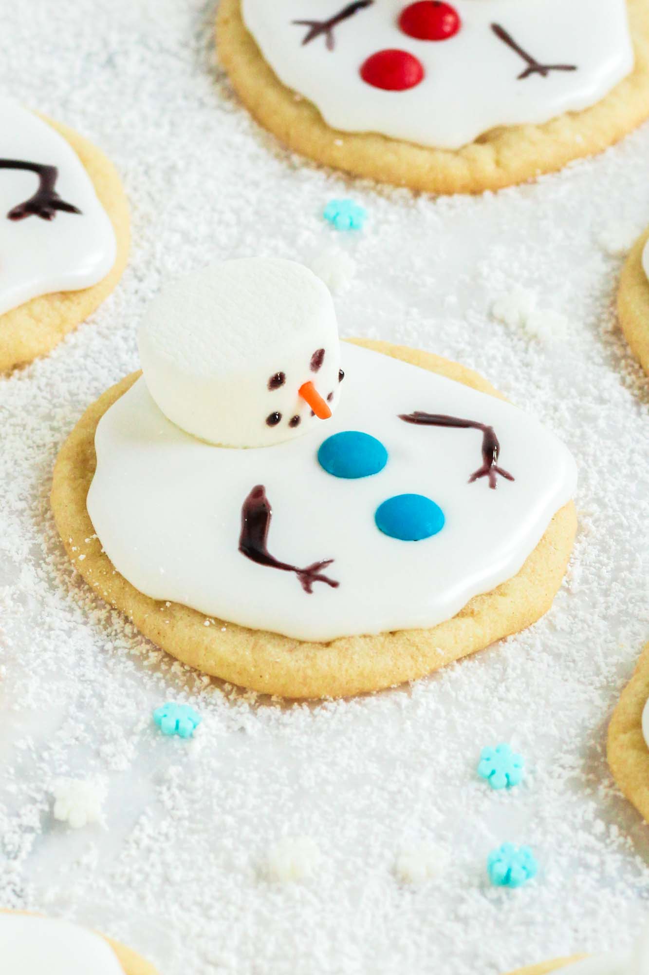 a round sugar cookie decorated with a marshmallow to look like a melting snowman. The cookie is sitting on a plate of sugar that looks like snow.
