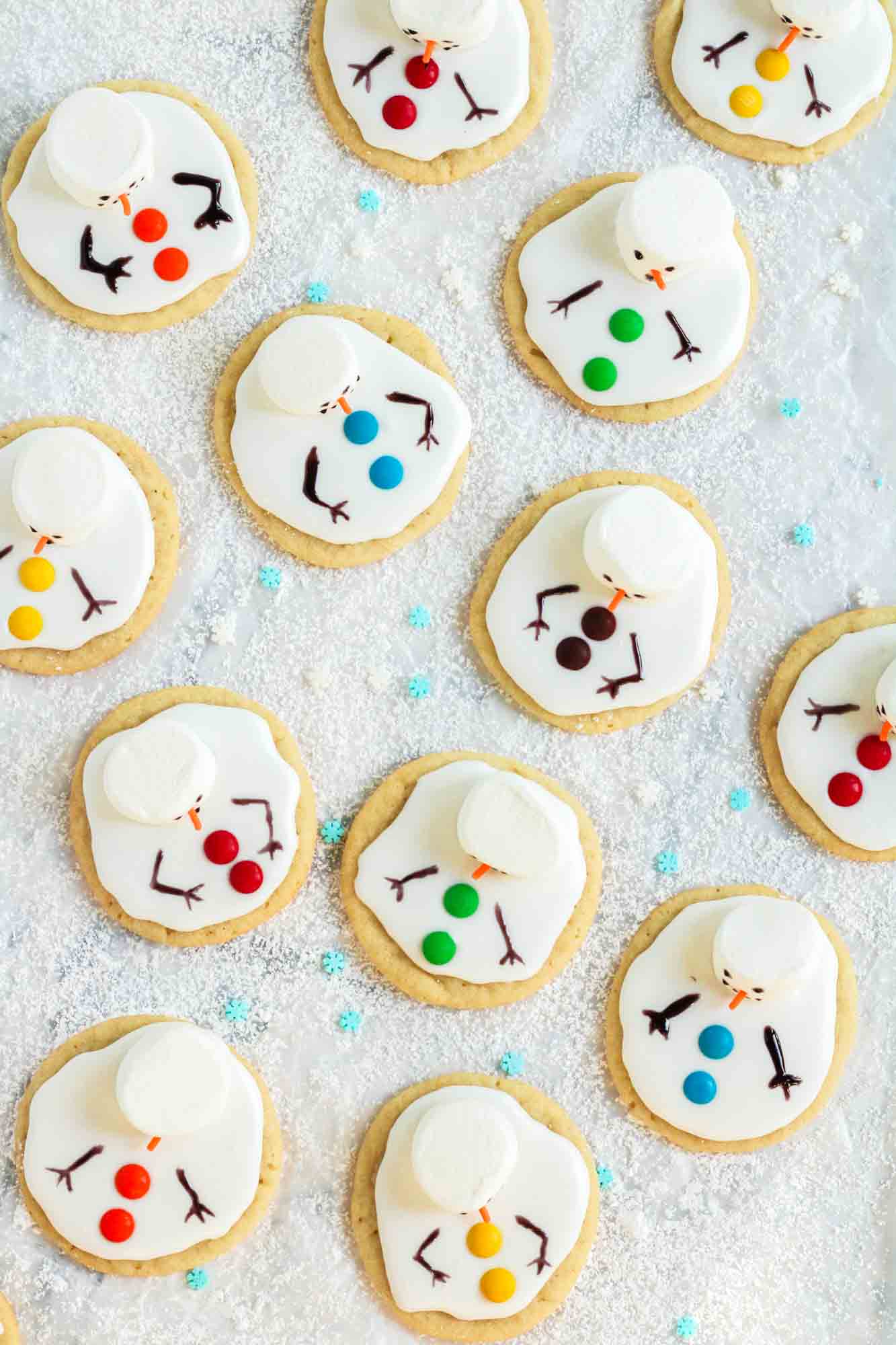 a group of melted snowman cookies on a tray of sugar and sprinkles meant to look like a snowy field.
