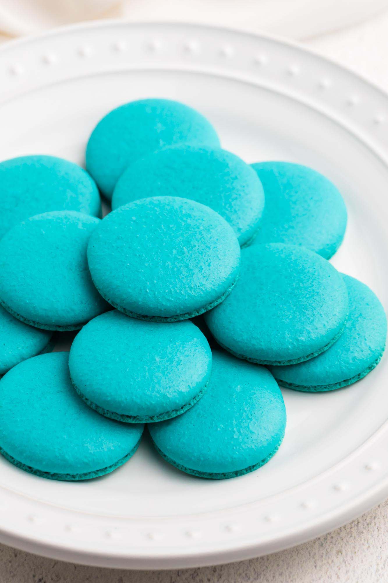 Teal blue baby yoda macaron sheels on a white plate without filling