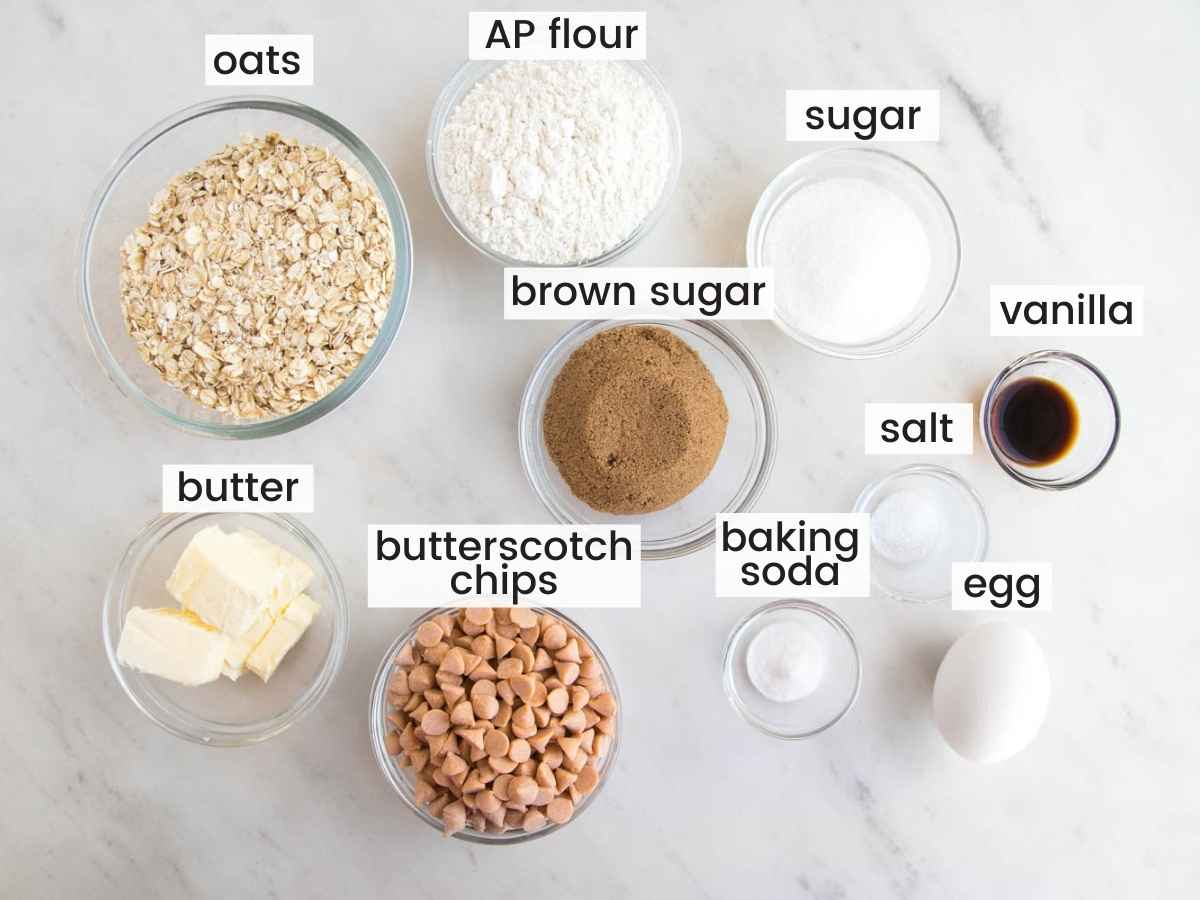 The ingredients for butterscotch oatmeal cookies all measured into separate bowls on a marble countertop