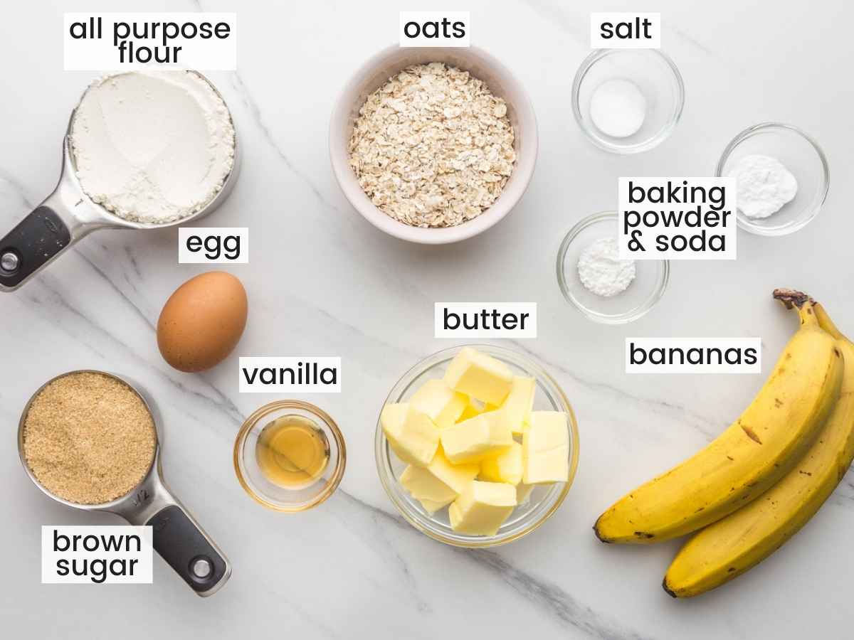 The ingredients for making soft banana bread cookies in separate bowls, laid out on a marble countertop