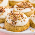 a raised plate filled with frosted banana bread cookies topped with chopped nuts
