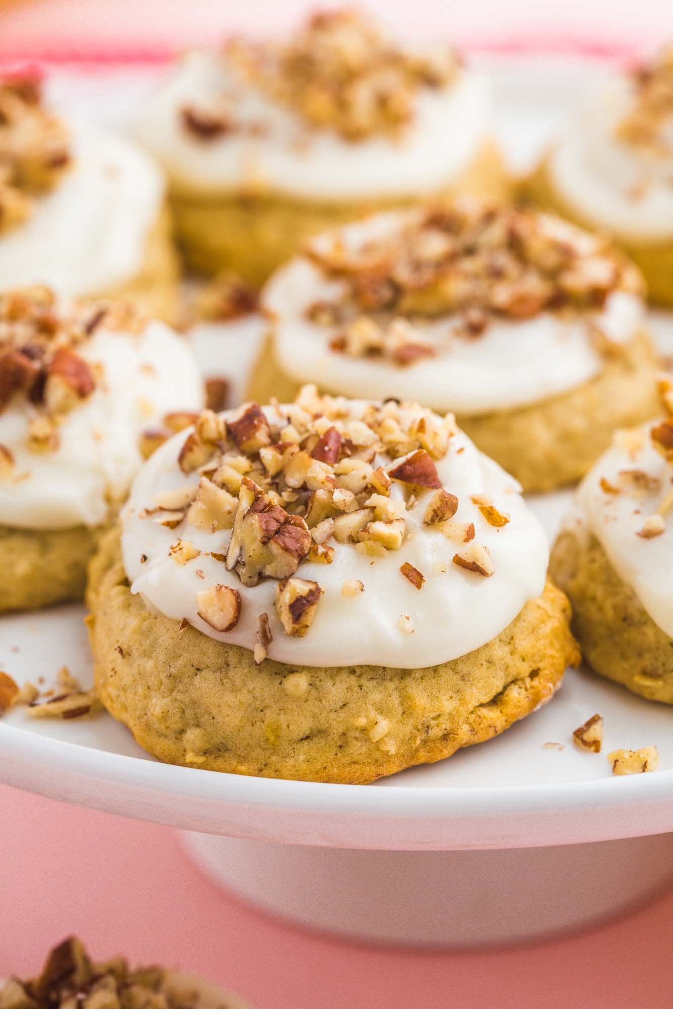 a raised plate filled with frosted banana bread cookies topped with chopped nuts