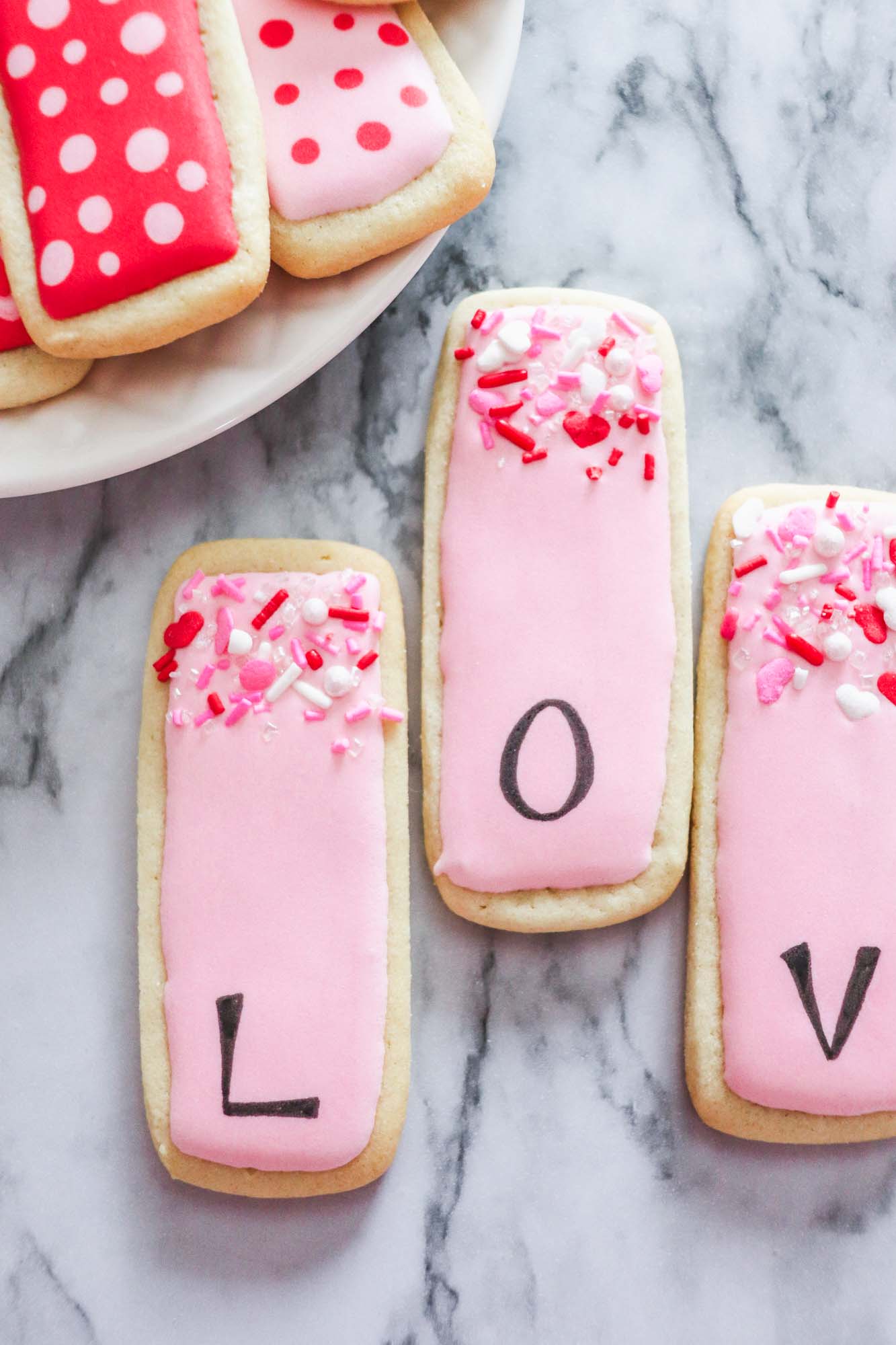 three rectangular cookies with letters L, O, V on them. Valentines themed sugar cookies with royal icing