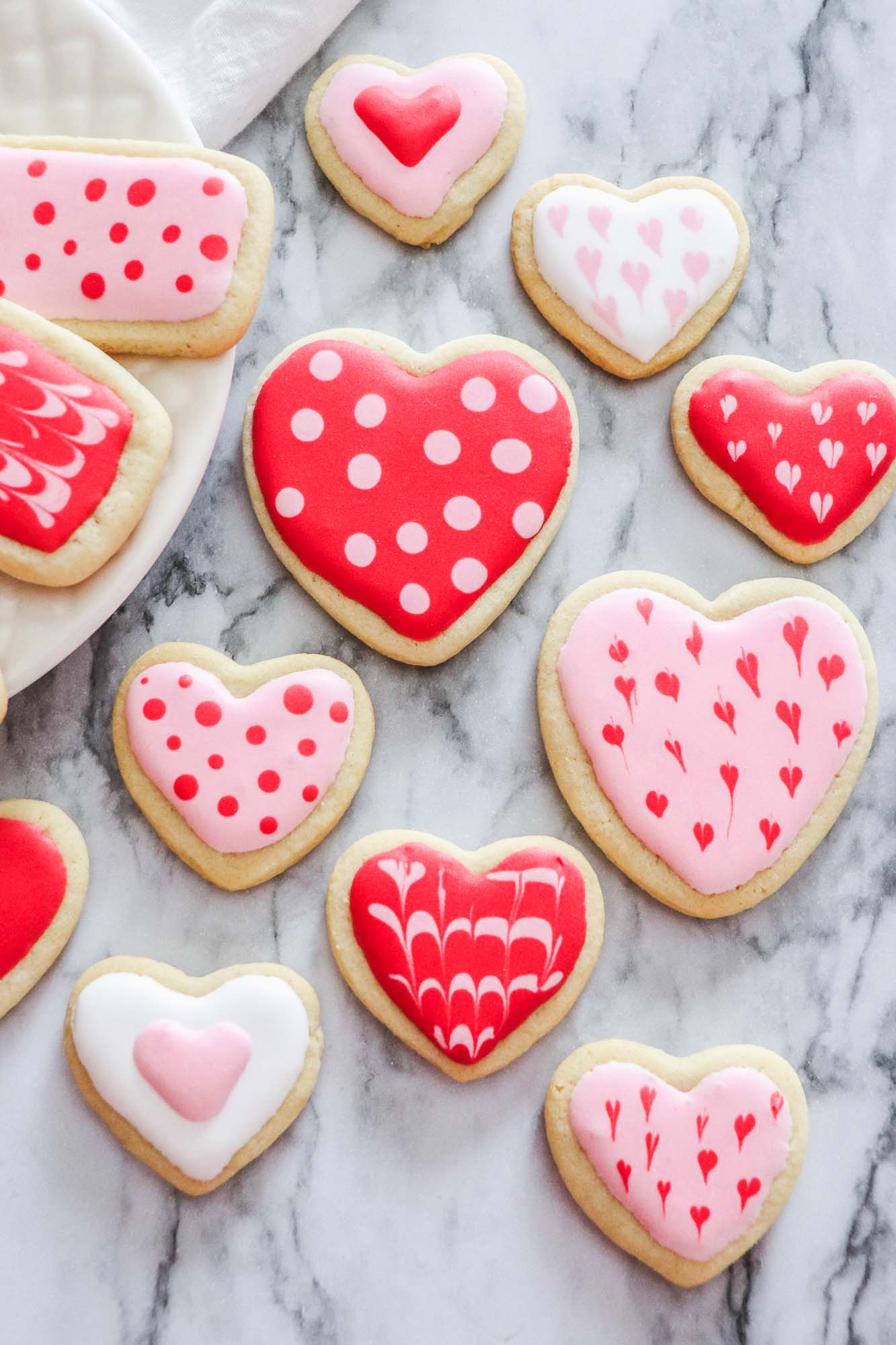 a variety of heart shaped cookies decorated with royal icing, sitting on a marble countertop