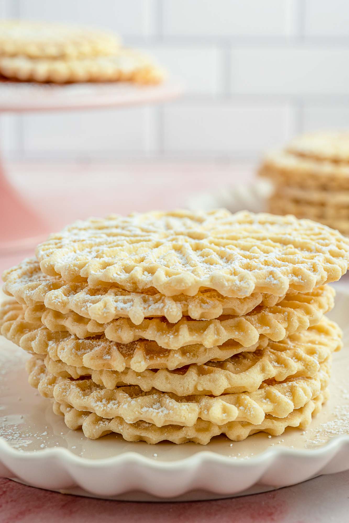 a stack of pizzelle cookies on a scalloped white plate.