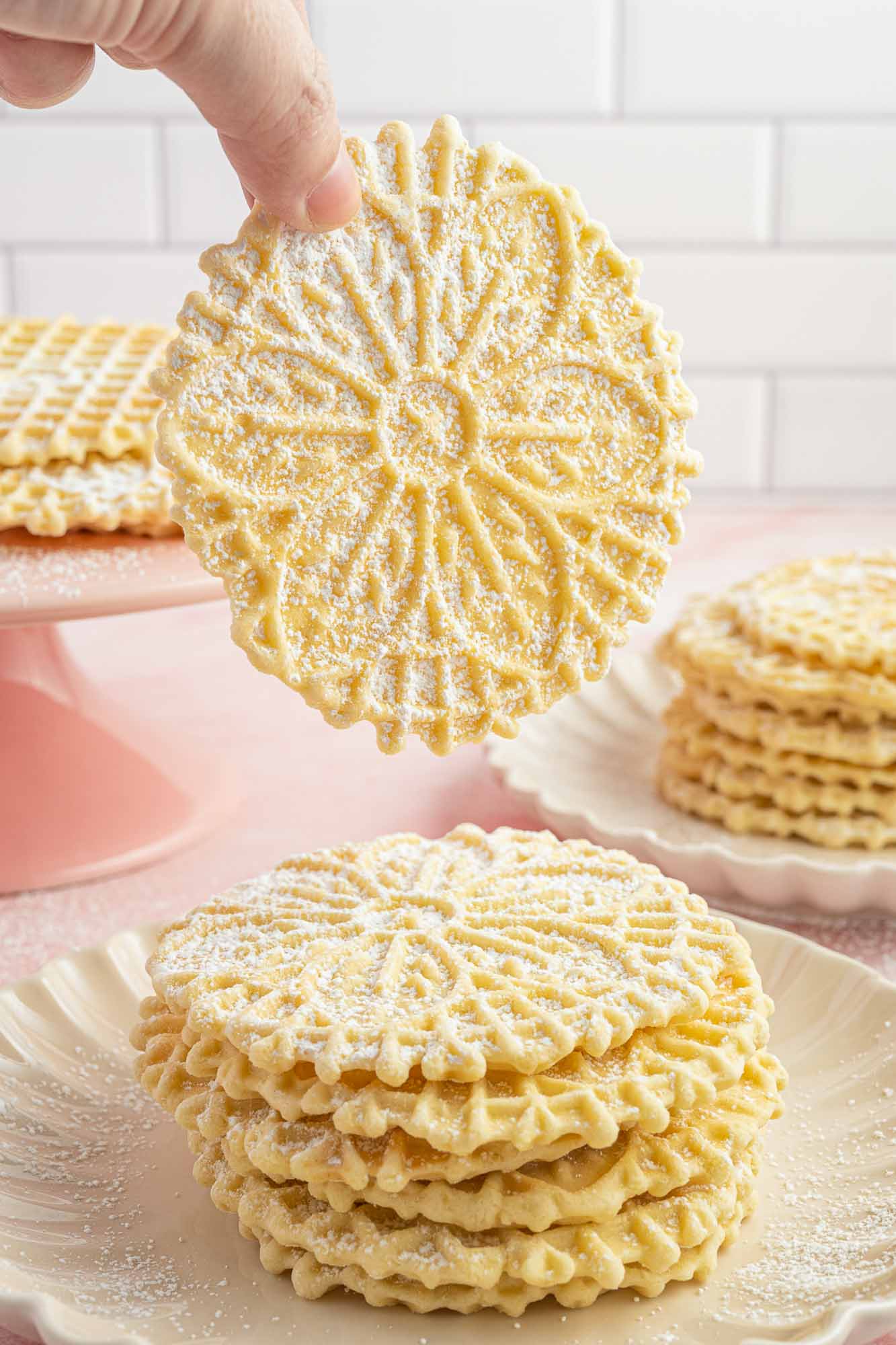 a hand picking up a floral patterned round pizzelle cookie from a stack. 