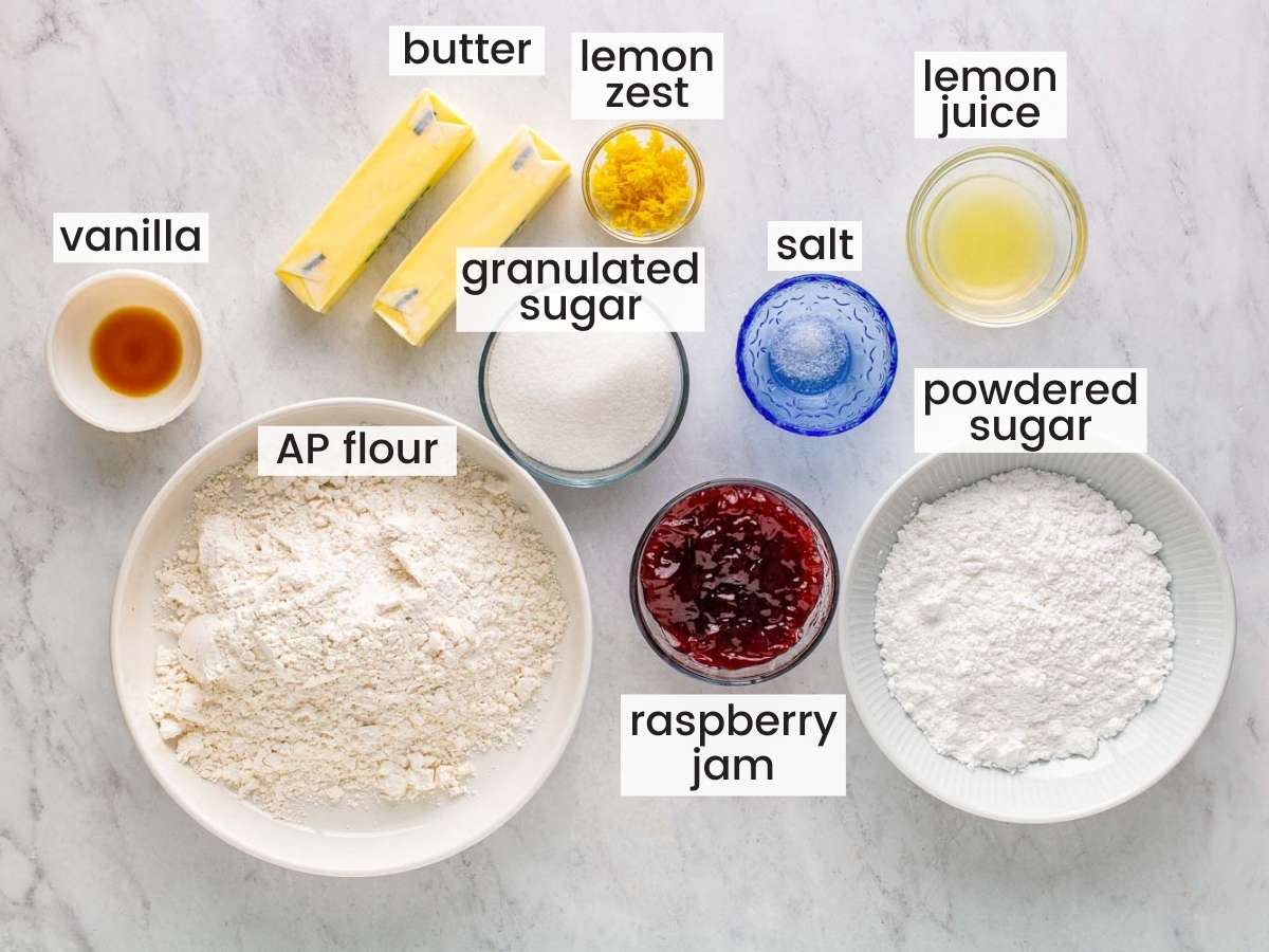 The ingredients for making raspberry thumbprint cookies, measured into separate bowls and set on a marble counter, viewed from above.