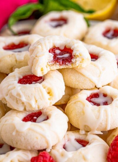 a stack of raspberry thumbprint cookies, one at the top has been bitten and replaced to show the inside texture.