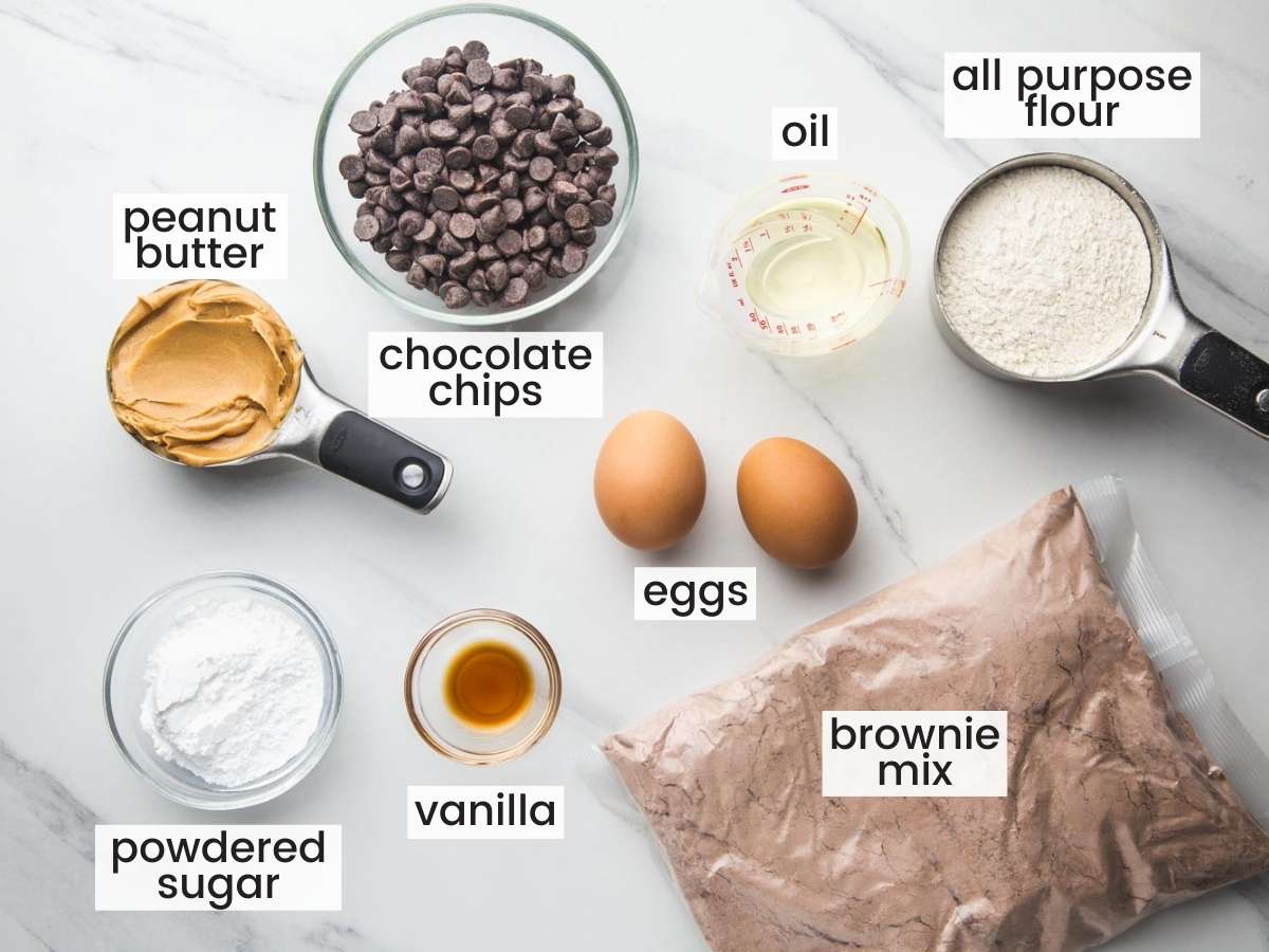 The ingredients for making buckeye brownie cookies, measured out and set on a counter. Included is the inside bag of a boxed brownie mix, chocolate chips, and peanut butter, plus other common baking supplies.