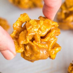 a hand holding a peanut butter cornflake cookie over a tray of cookies.