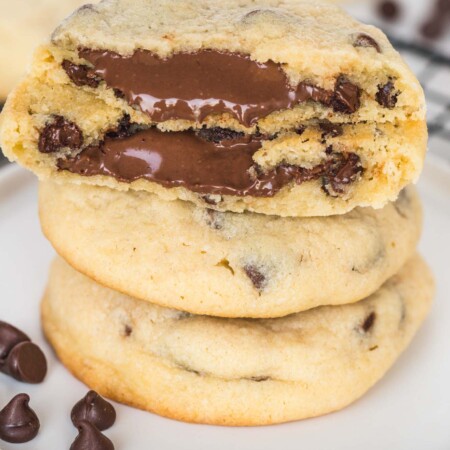 a stack of three chocolate chip cookies. the top one is split in half and melty nutella is oozing out.