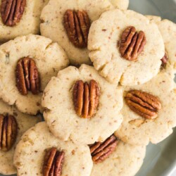 a plate of homemade pecan sandies cookies with whole nuts on top of each.