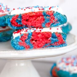 2 patriotic cookies frosted and served on a small white cake stand.