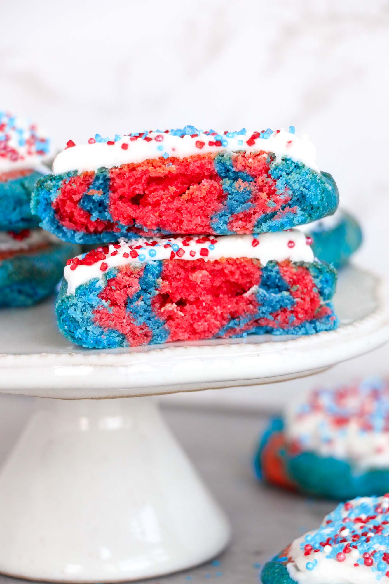 2 patriotic cookies frosted and served on a small white cake stand.