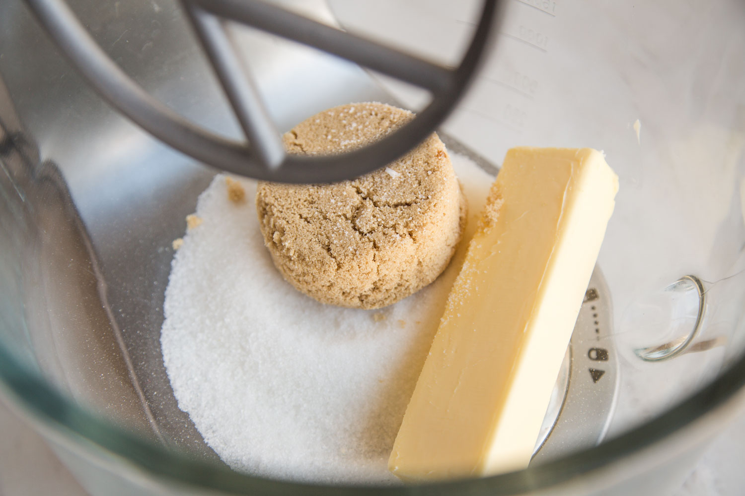 A stick of butter, and sugars in a bowl of a stand mixer.