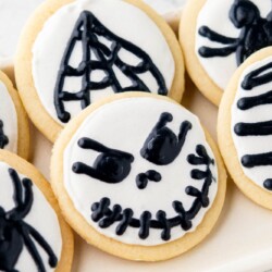 round cut out cookies with white icing and black halloween decorations, skulls and spiders