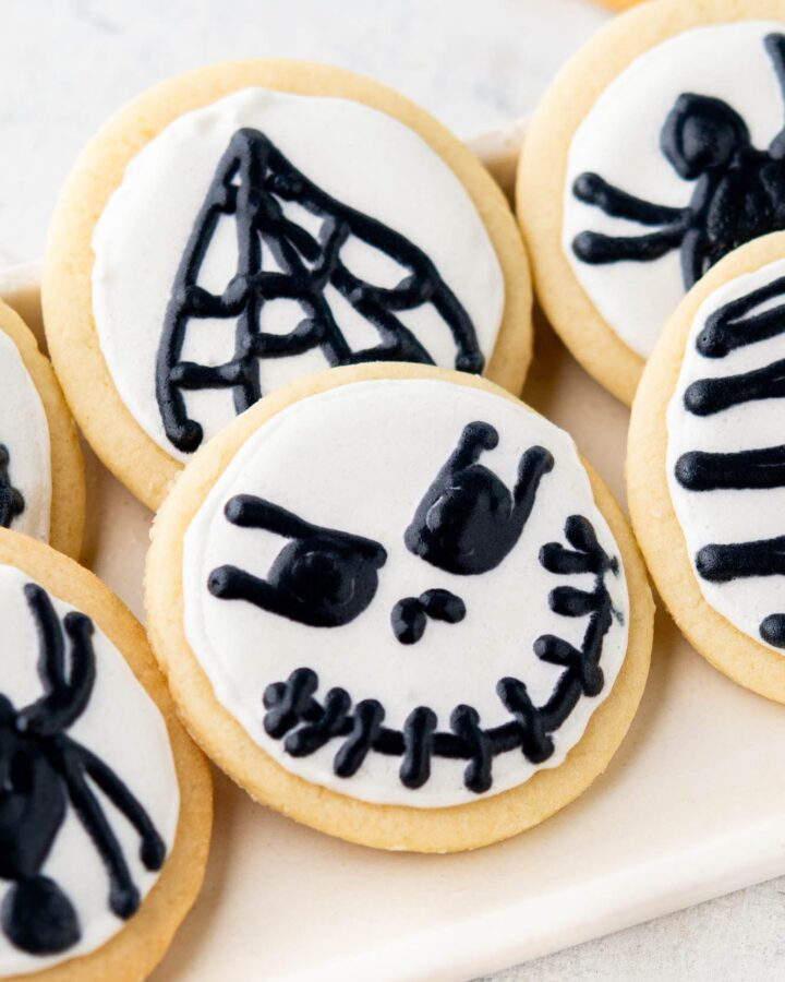 round cut out cookies with white icing and black halloween decorations, skulls and spiders