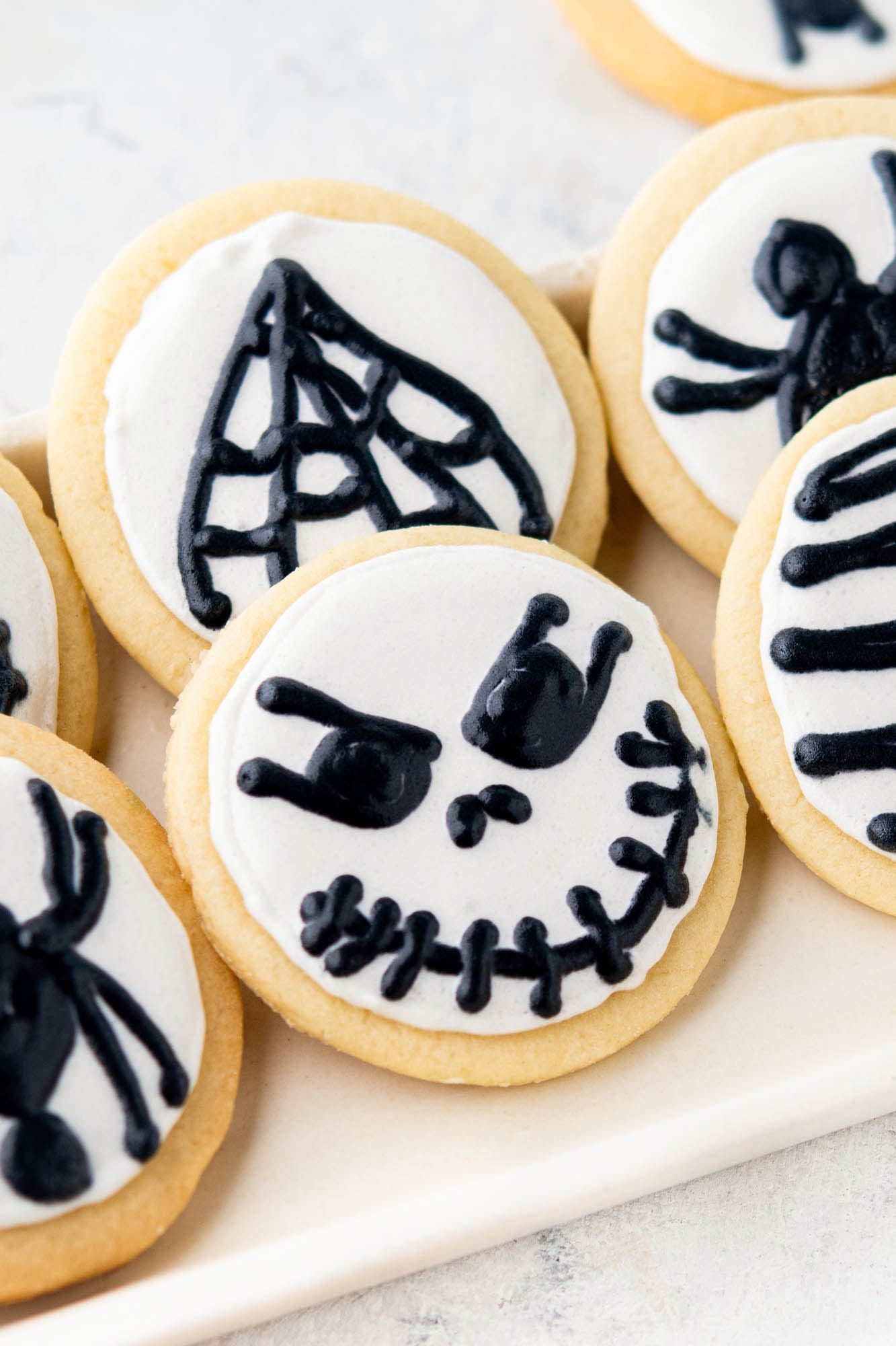round cut out cookies with white icing and black halloween decorations, skulls and spiders
