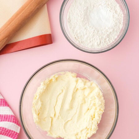 Creamed butter and sugar in a glass bowl, and a bowl with flour on the side, and a rolling pin with a silicone mat.