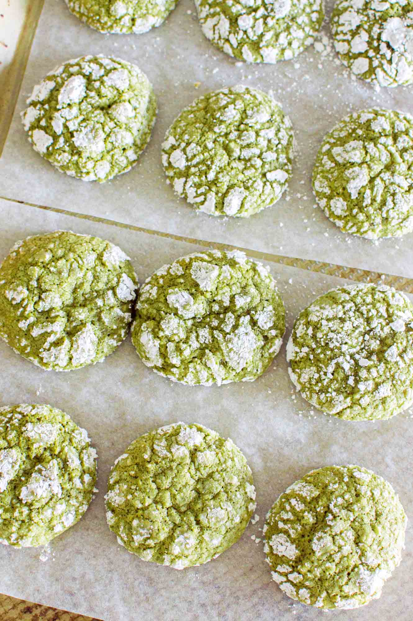 Overhead shot of matcha crinkle cookies on a cookie sheet with parchment paper