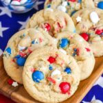 Red white and blue M&M cookies placed on a wooden plate, with USA flag in the background.