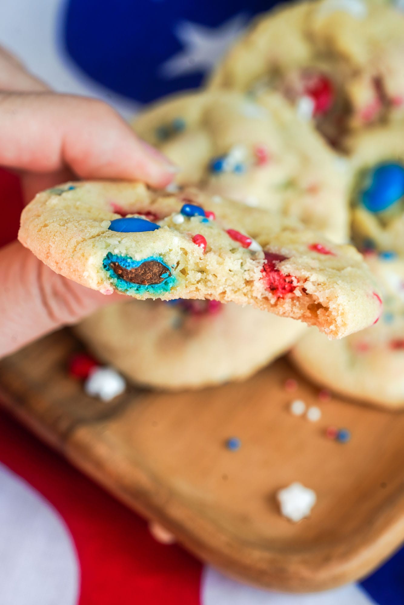 A bite shot of M&M patriotic cookie, holding it with a hand.