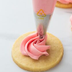 Decorating a sugar cookie with pink buttercream using a piping bag with a star tip