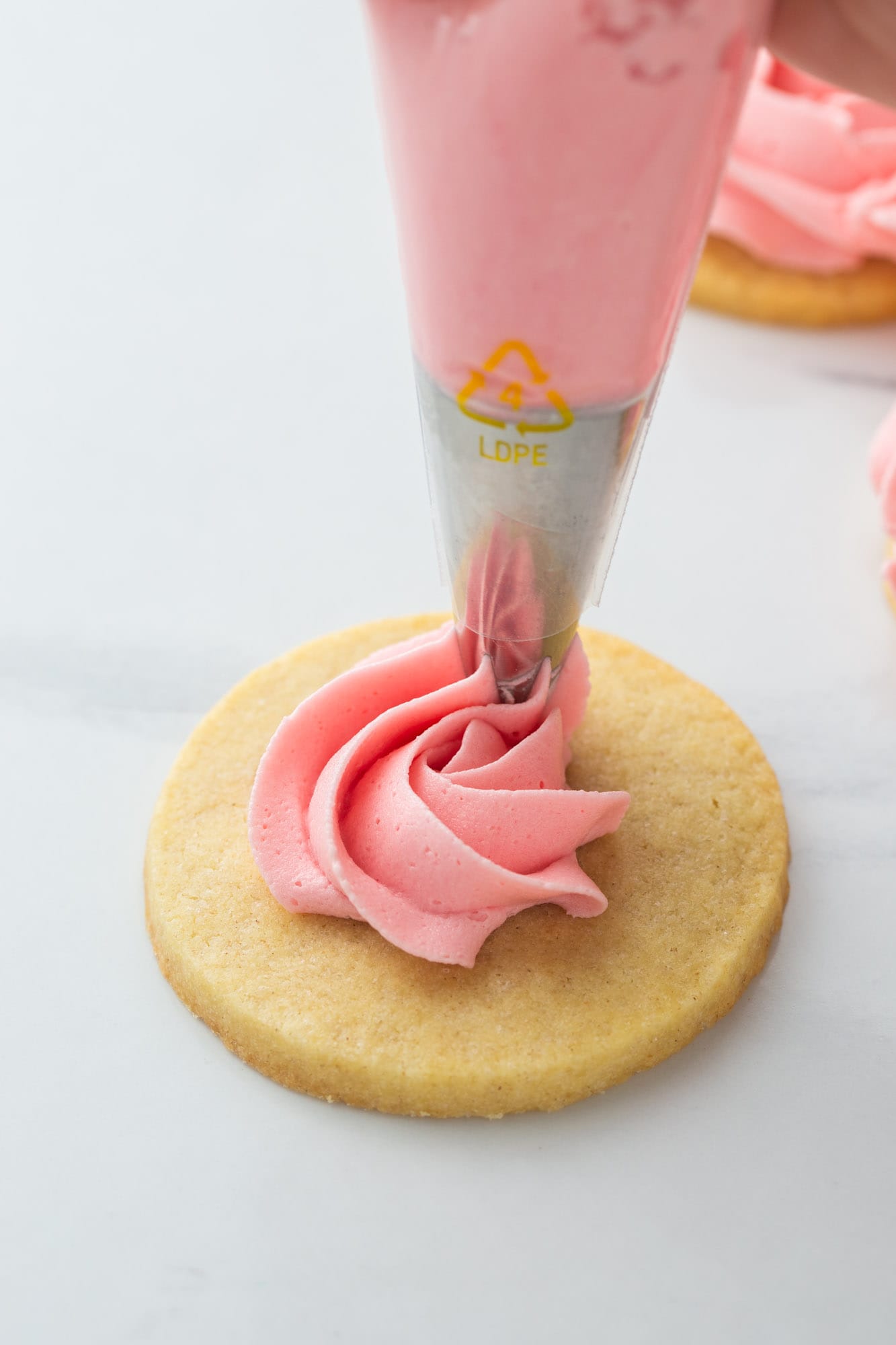 Decorating a sugar cookie with pink buttercream using a piping bag with a star tip