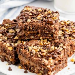 Squares of caramel and walnut brownies are staked on a white plate