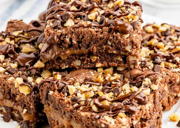 Squares of caramel and walnut brownies are staked on a white plate