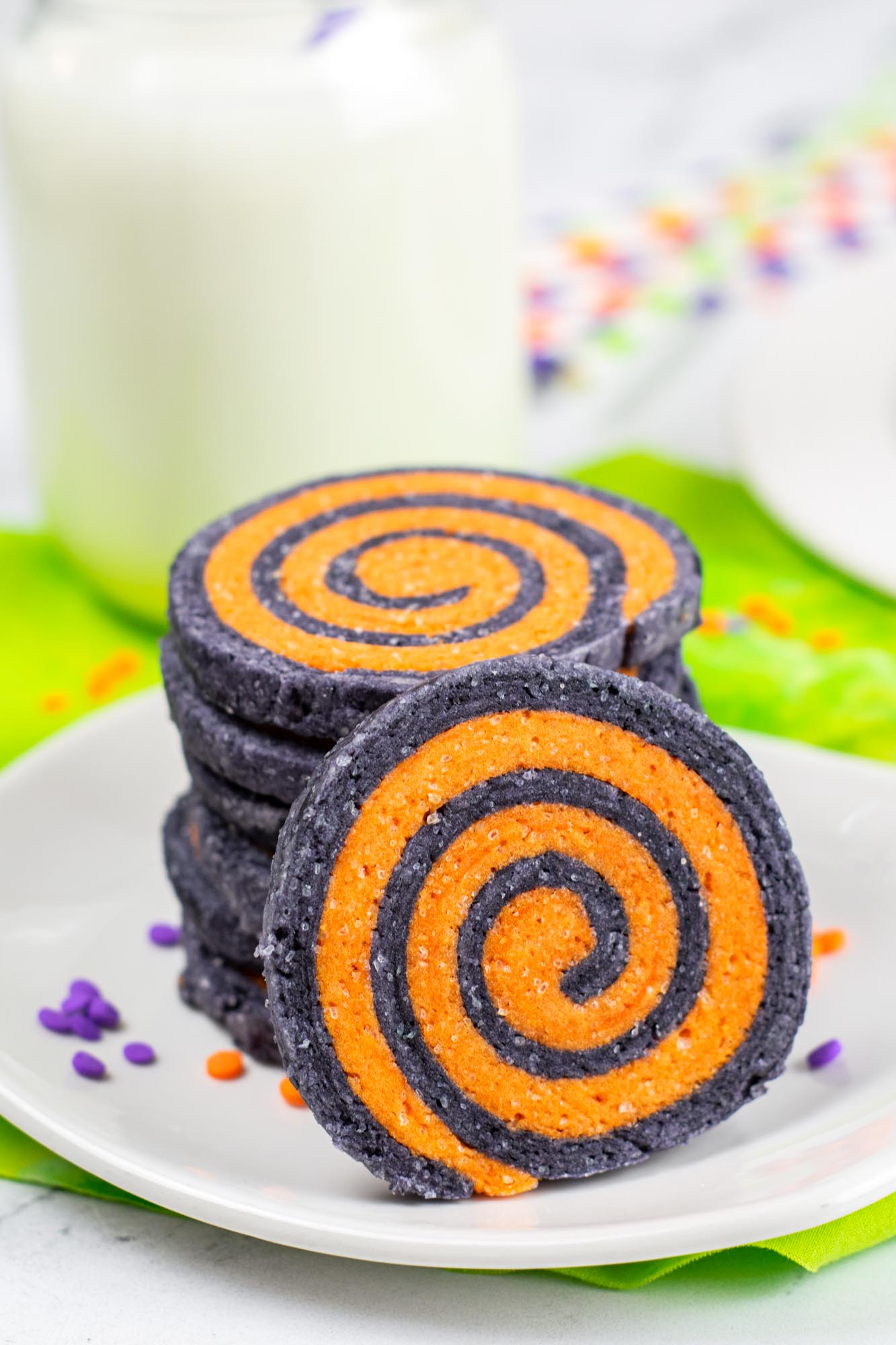 stack of halloween cookies on a white plate with a glass of milk behind them 