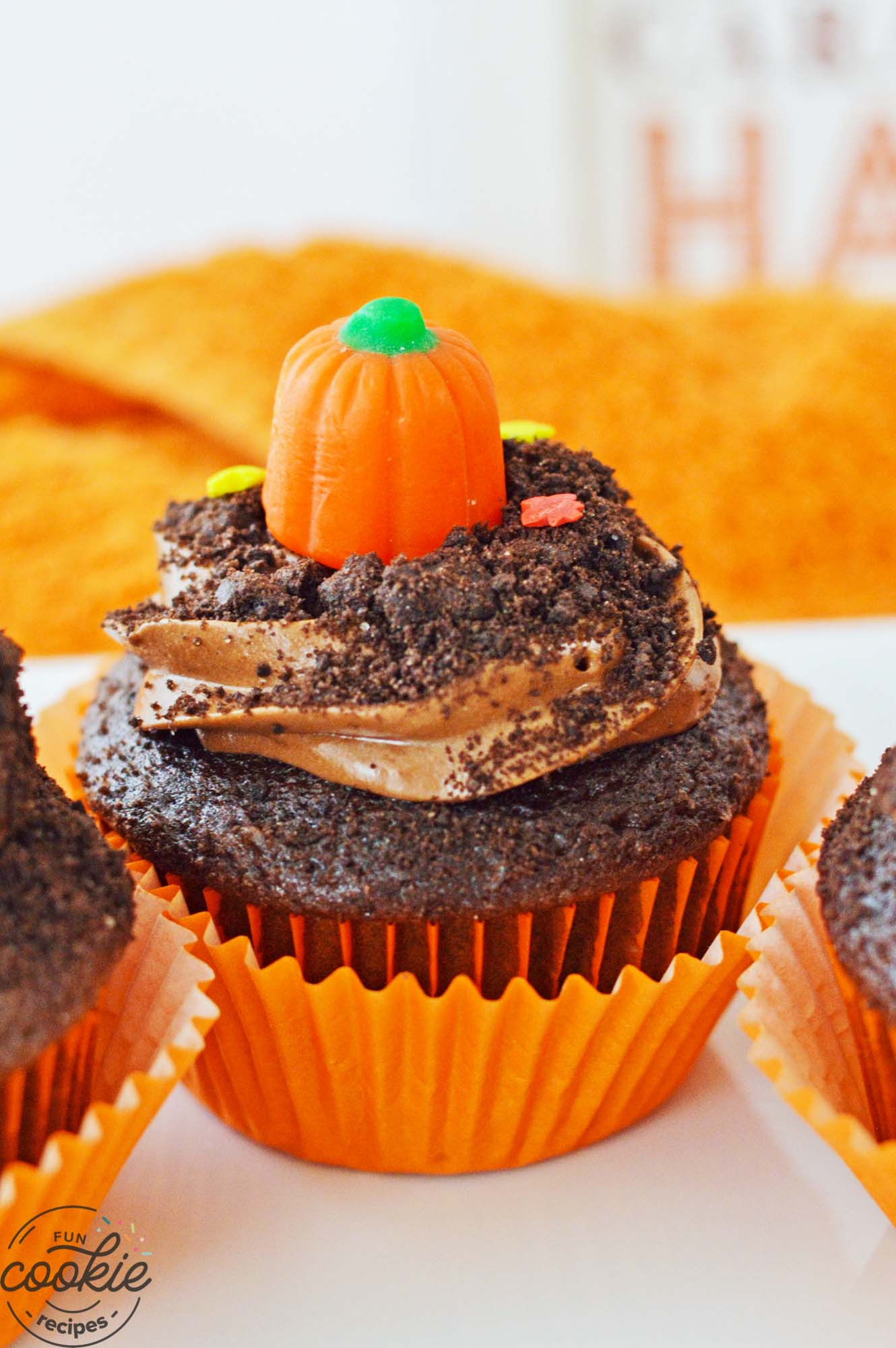 Close up shot of a pumpkin patch cupcake with orange wrapper, and a pumpkin candy on top.