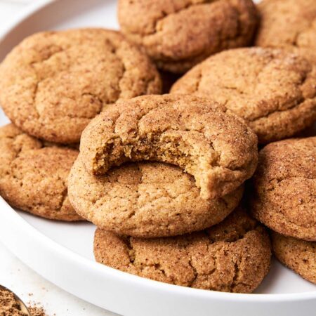 a round lipped plate filled with pumpkin snickerdoodles. A bit has been taken out of one of the cookies on the top of the pile.