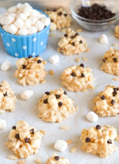 Avalanche cookies placed on a pan with parchment paper, and mini marshmallows in a blue bowl in the background.