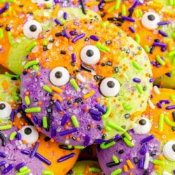 Closeup view of a purple, green, and orange sugar cookie with halloween sprinkles and candy eyes.
