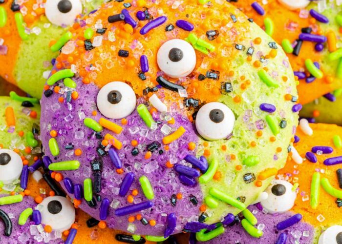 Closeup view of a purple, green, and orange sugar cookie with halloween sprinkles and candy eyes.