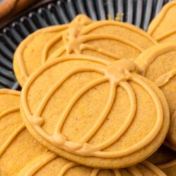Close up shot of pumpkin cut out sugar cookies on a black plate